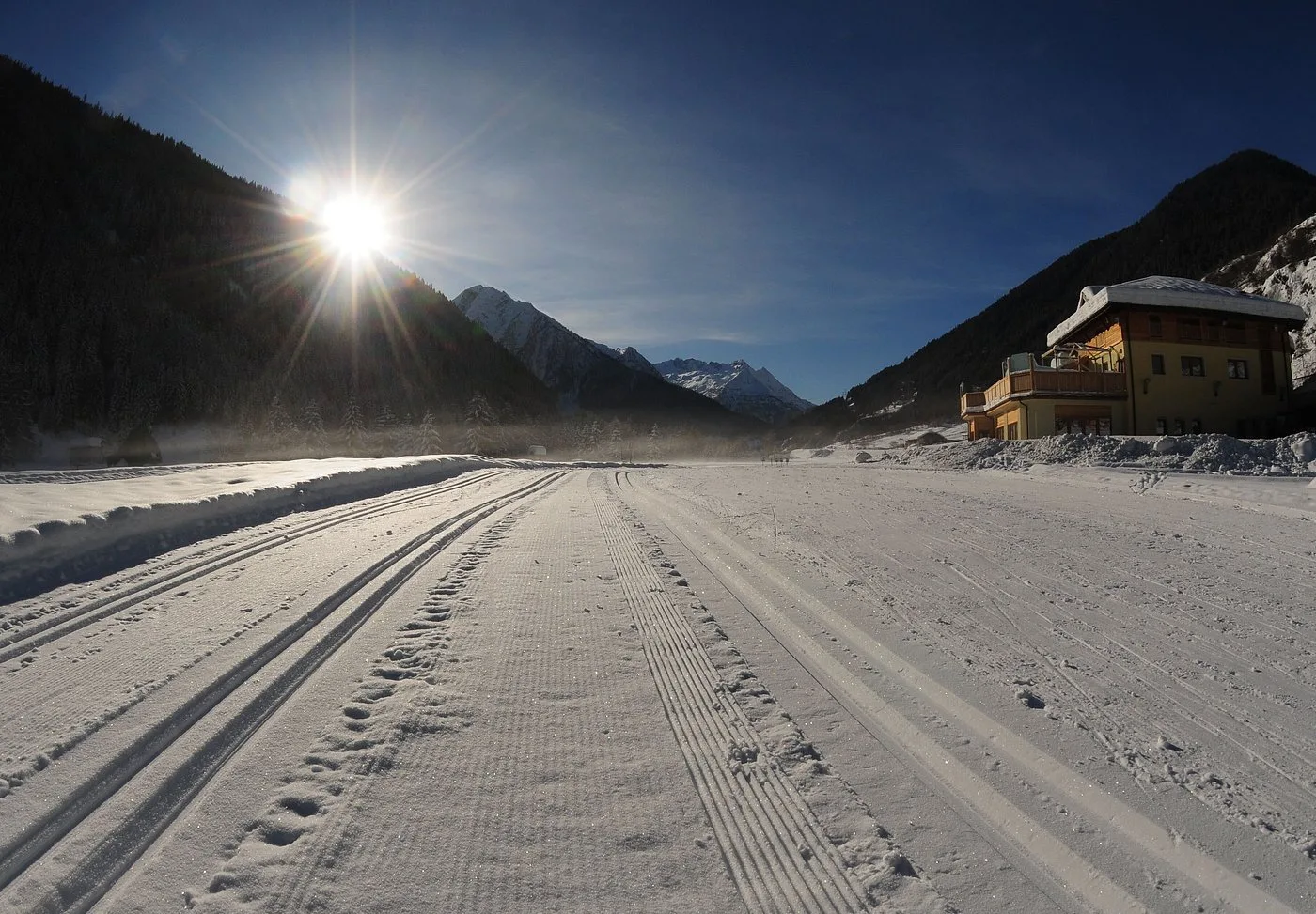 Pista da sci di fondo battuta al sole con montagne e hotel sullo sfondo