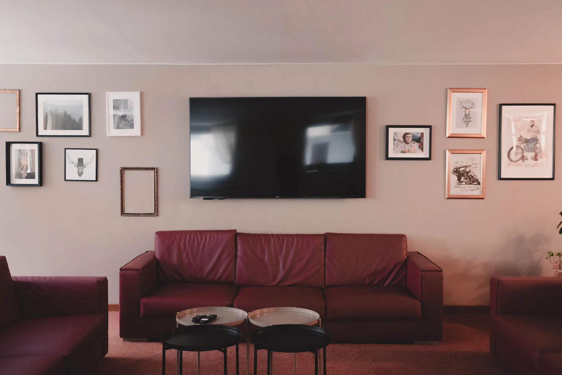 Salotto con divani in pelle bordeaux, TV a parete e quadri decorativi