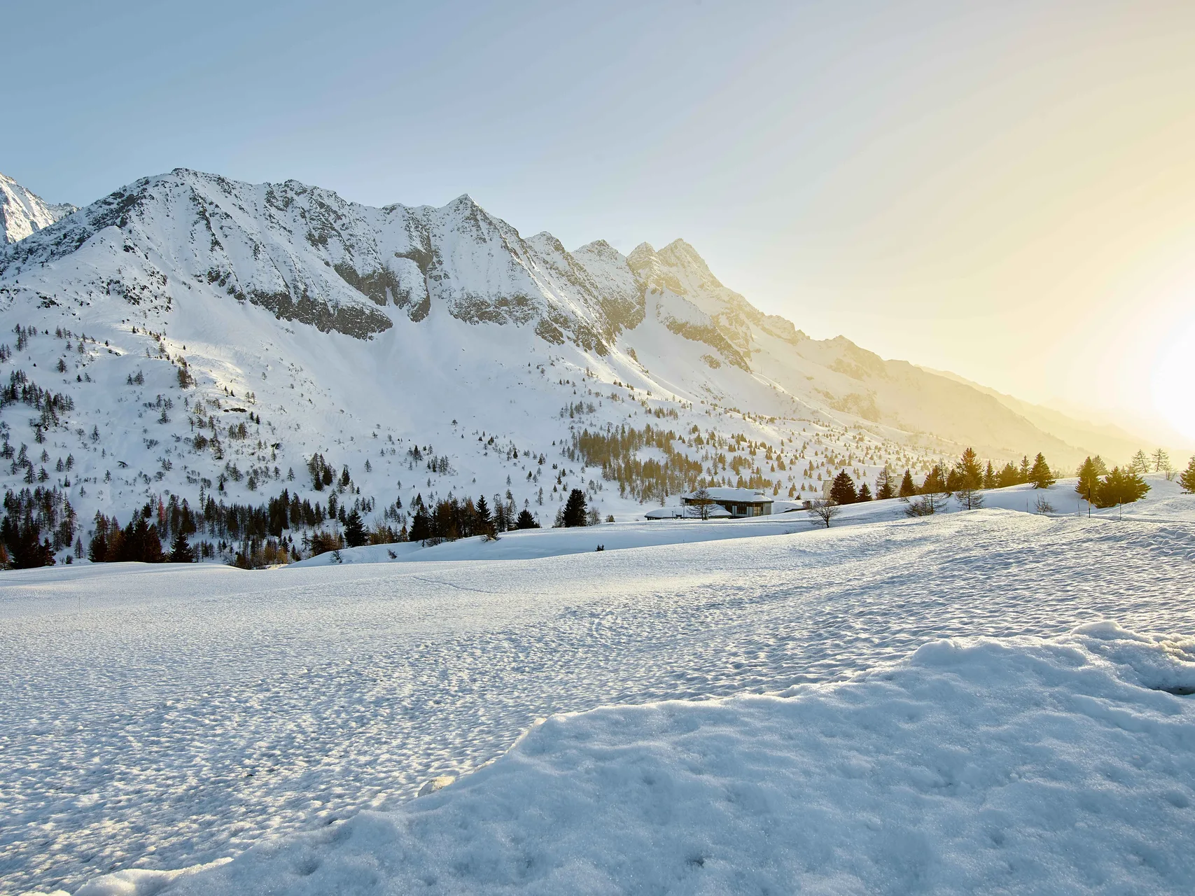 Vallata alpina innevata con montagne e sole al tramonto