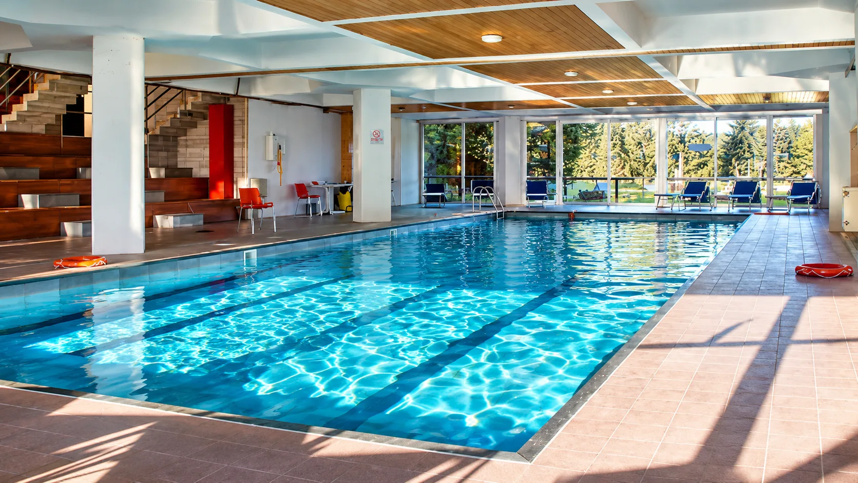 Piscina interna con soffitto in legno, colonne bianche e vetrate sul verde