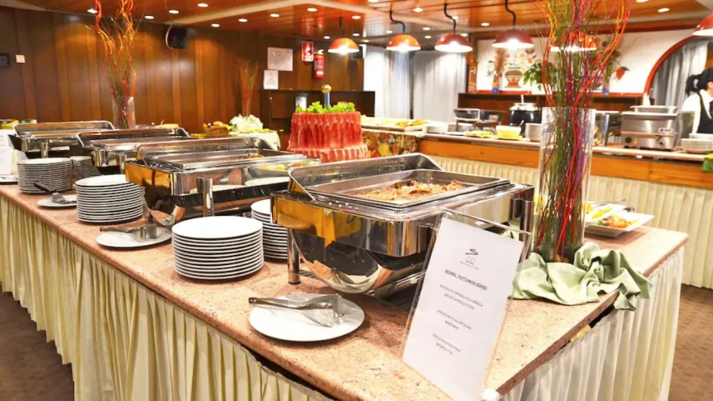 Buffet del ristorante con vassoi caldi, piatti impilati e decorazioni floreali