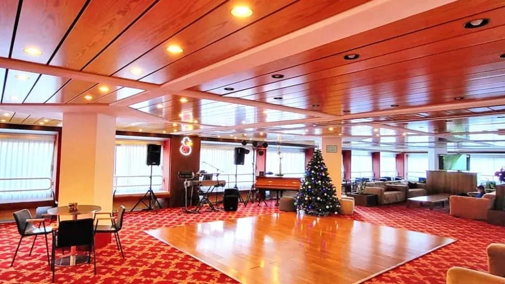 Sala comune con pista da ballo in legno, pianoforte, albero di Natale e moquette rossa