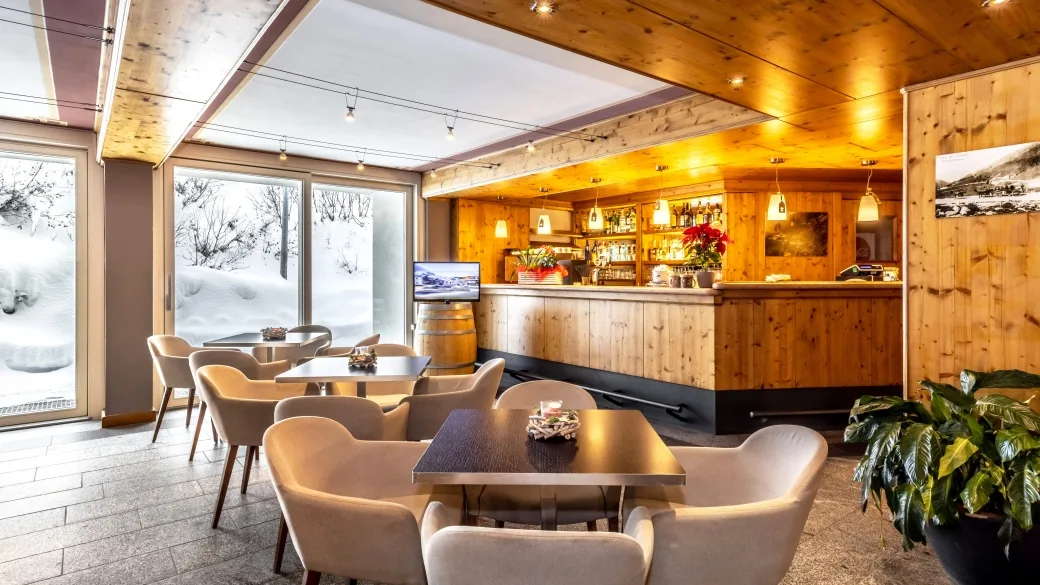 Bar dell'hotel con bancone in legno, tavoli e poltrone moderne e ampie vetrate affacciate sulla neve