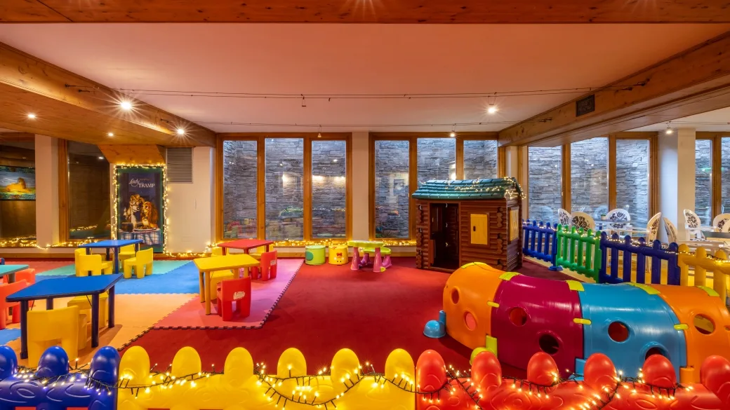 Sala giochi per bambini colorata con tavolini, casetta e giochi morbidi, illuminata da luci festose