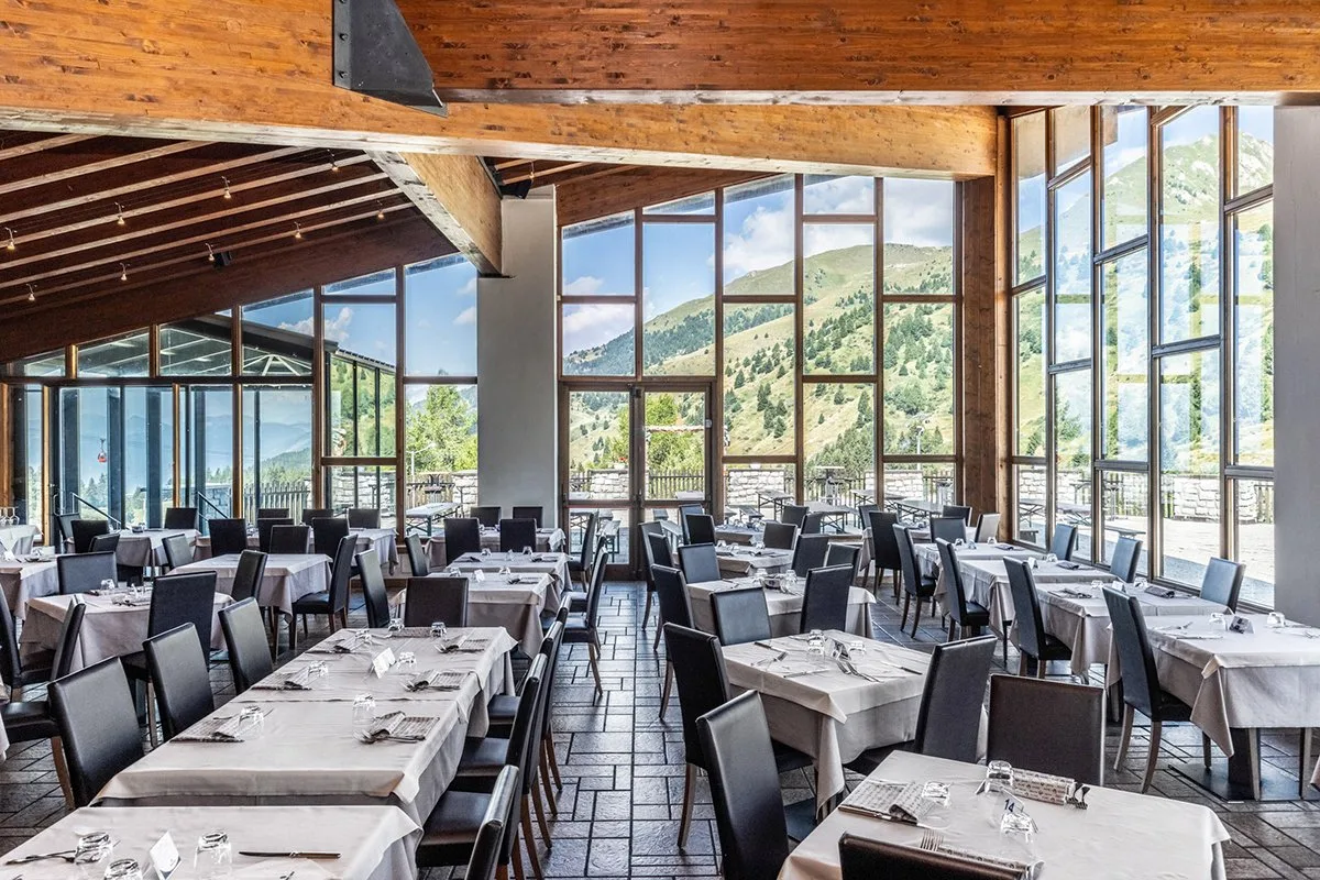 Sala ristorante con tavoli apparecchiati e ampie vetrate sulle montagne verdi