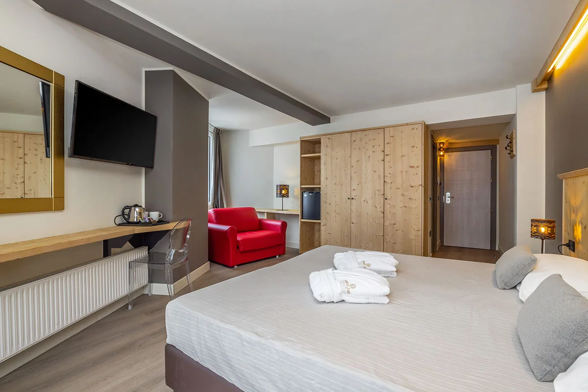 Ampia camera con letto matrimoniale, poltrona rossa, TV e armadio in legno