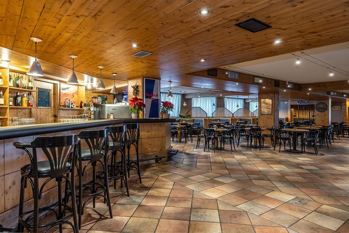 Sala bar in stile alpino con bancone in legno, sgabelli e tavoli