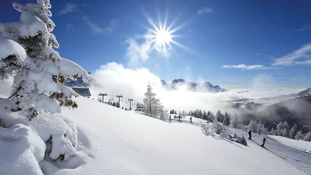 Panorama di montagna innevata con sole splendente, sciatori e impianti di risalita
