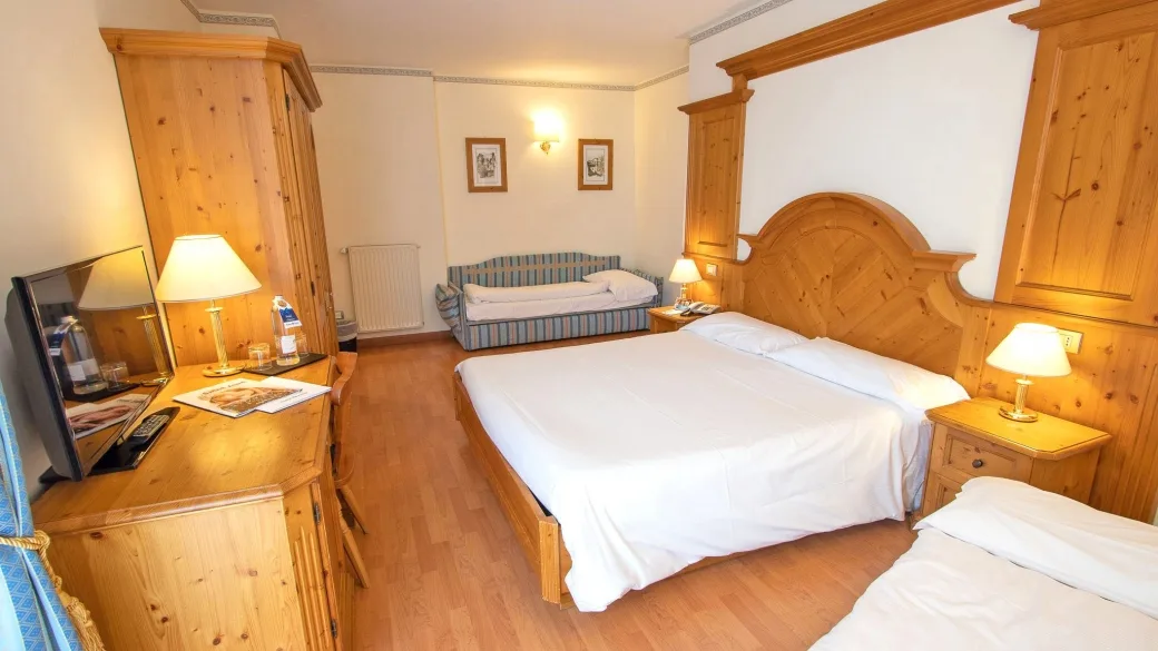 Camera da letto con arredi in legno chiaro, letto matrimoniale, divano e TV