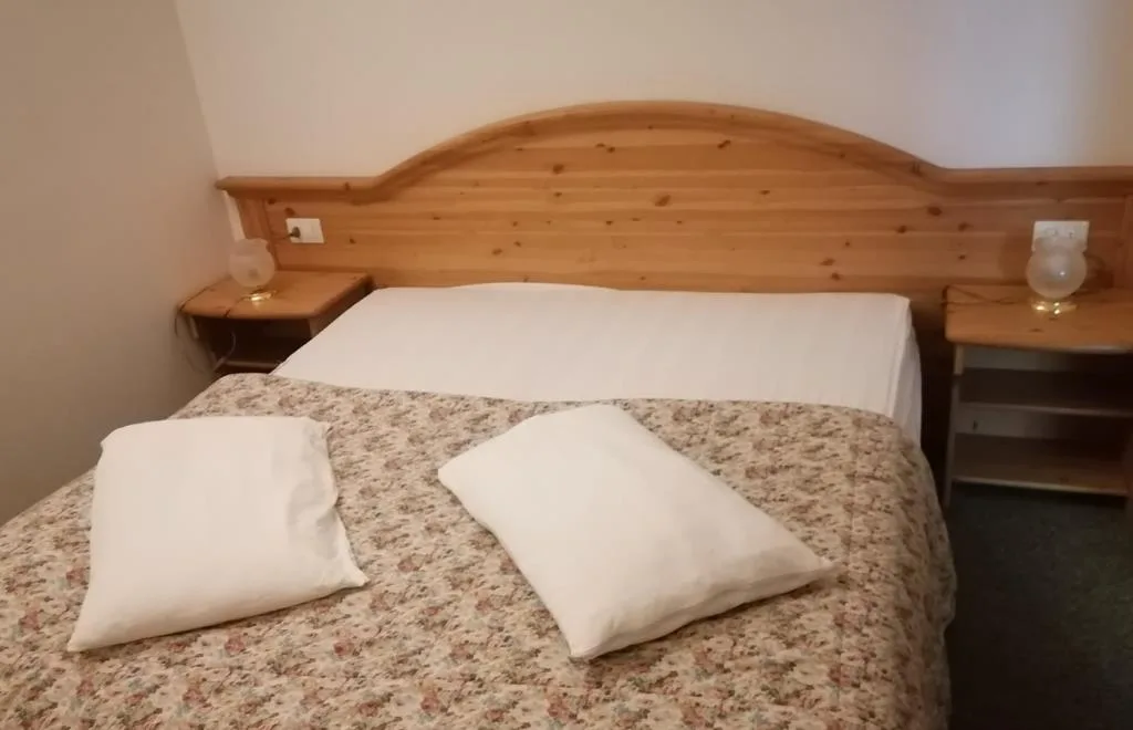 Letto matrimoniale con testiera in legno, cuscini bianchi e comodini con lampade