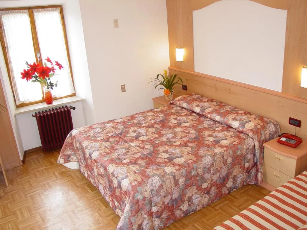 Camera matrimoniale con testiera in legno, copriletto floreale e finestra con fiori