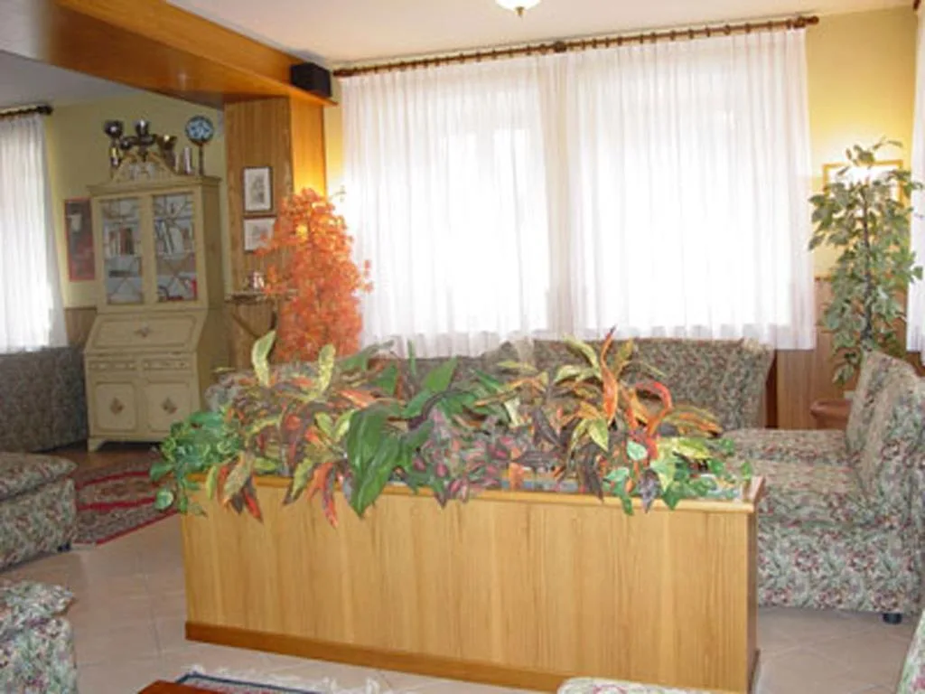 Salotto dell'hotel con poltrone a fiori, piante e ampie finestre con tende bianche